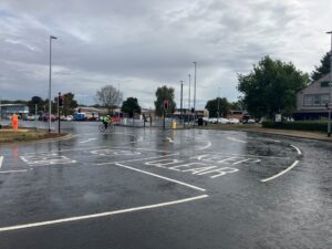 The corner of a junction on to a main road controlled by traffic lights. There is a new road surface and new road markings.