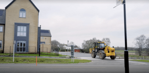 A new build house with a yellow construction tractor driving on the road alongside it.