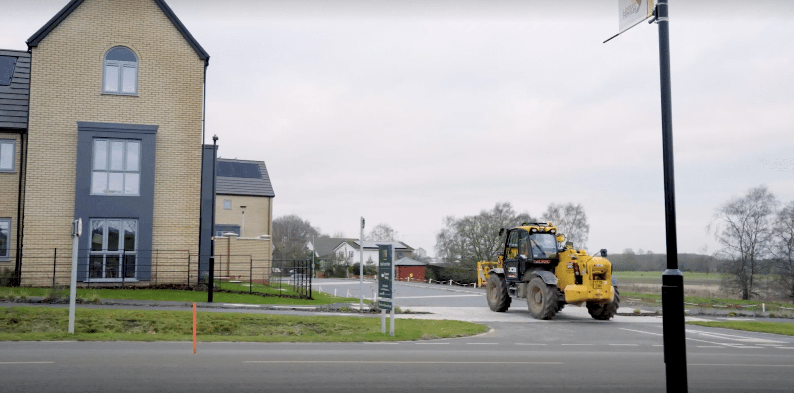 A new build house with a yellow construction tractor driving on the road alongside it.